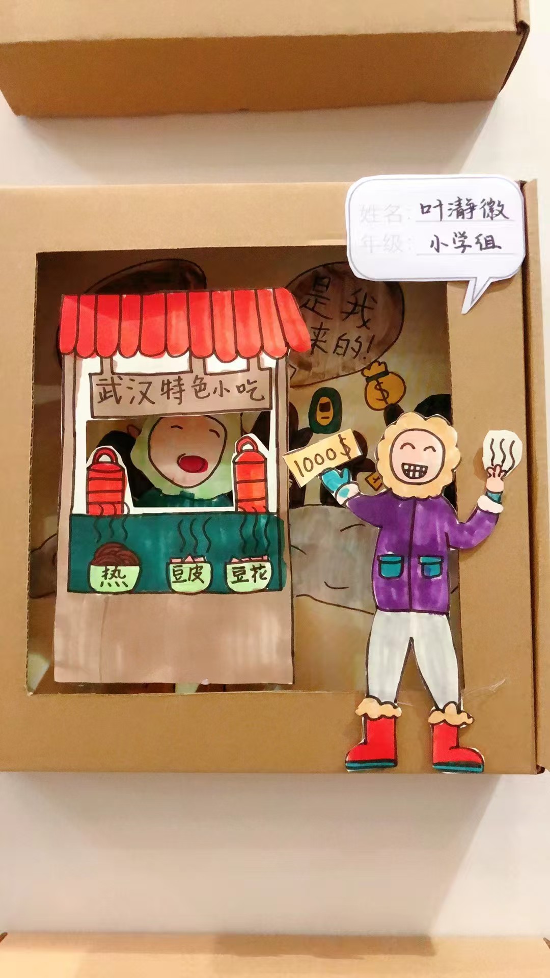 Student artwork of a street food scene in a cardboard display box